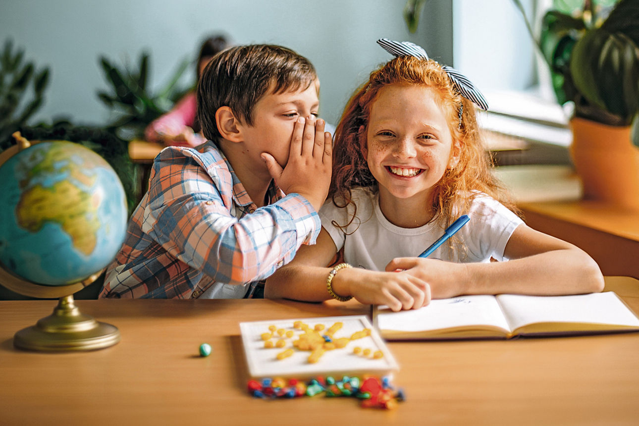 Junge und Mädchen sitzend am Tisch in einem Klassenzimmer