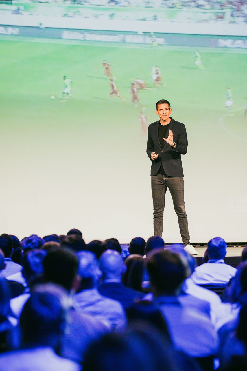 Deniz Aytekin steht bei einem Vortrag vor einer Leinwand mit einem Fußballspiel