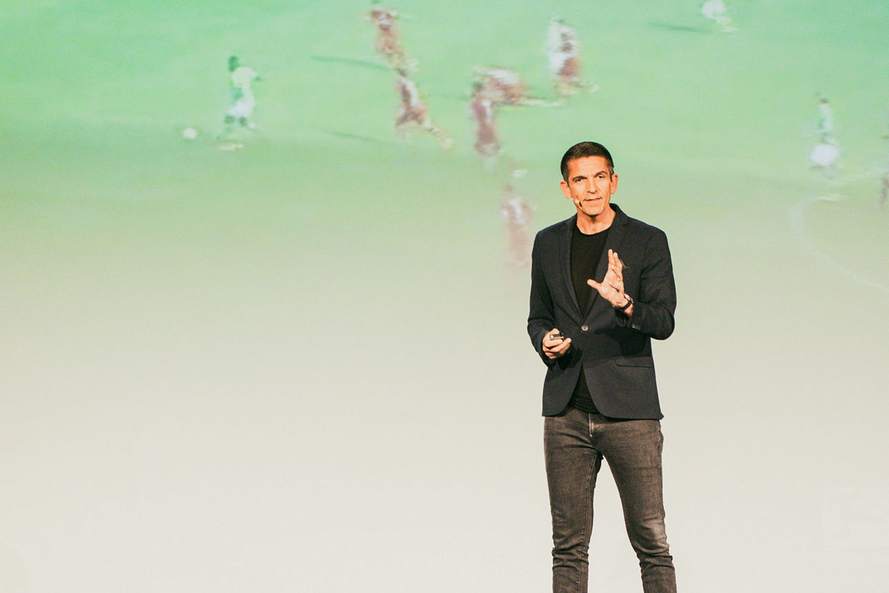Deniz Aytekin steht bei einem Vortrag vor einer Leinwand mit einem Fußballspiel