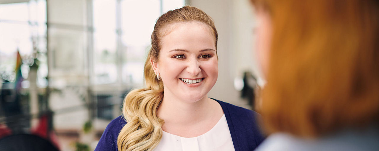 Eine blonde, junge Frau lächelt ihre Kollegin an. 