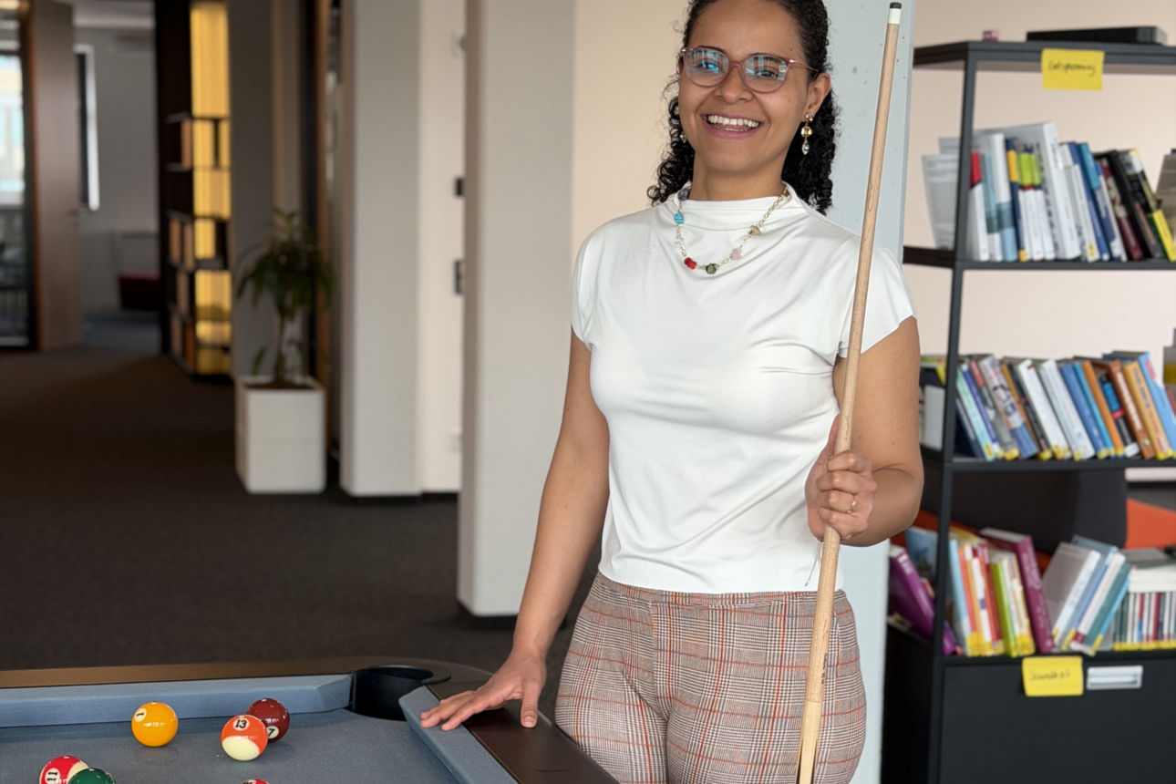 Junge Frau steht neben einem Billard-Tisch und lächelt