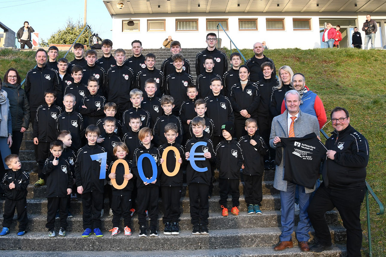 Eine große Gruppe Jungs und Mädchen steht versetzt auf einer Treppe und hält in blau-orangen Zeichen 7.000 € in die Höhe