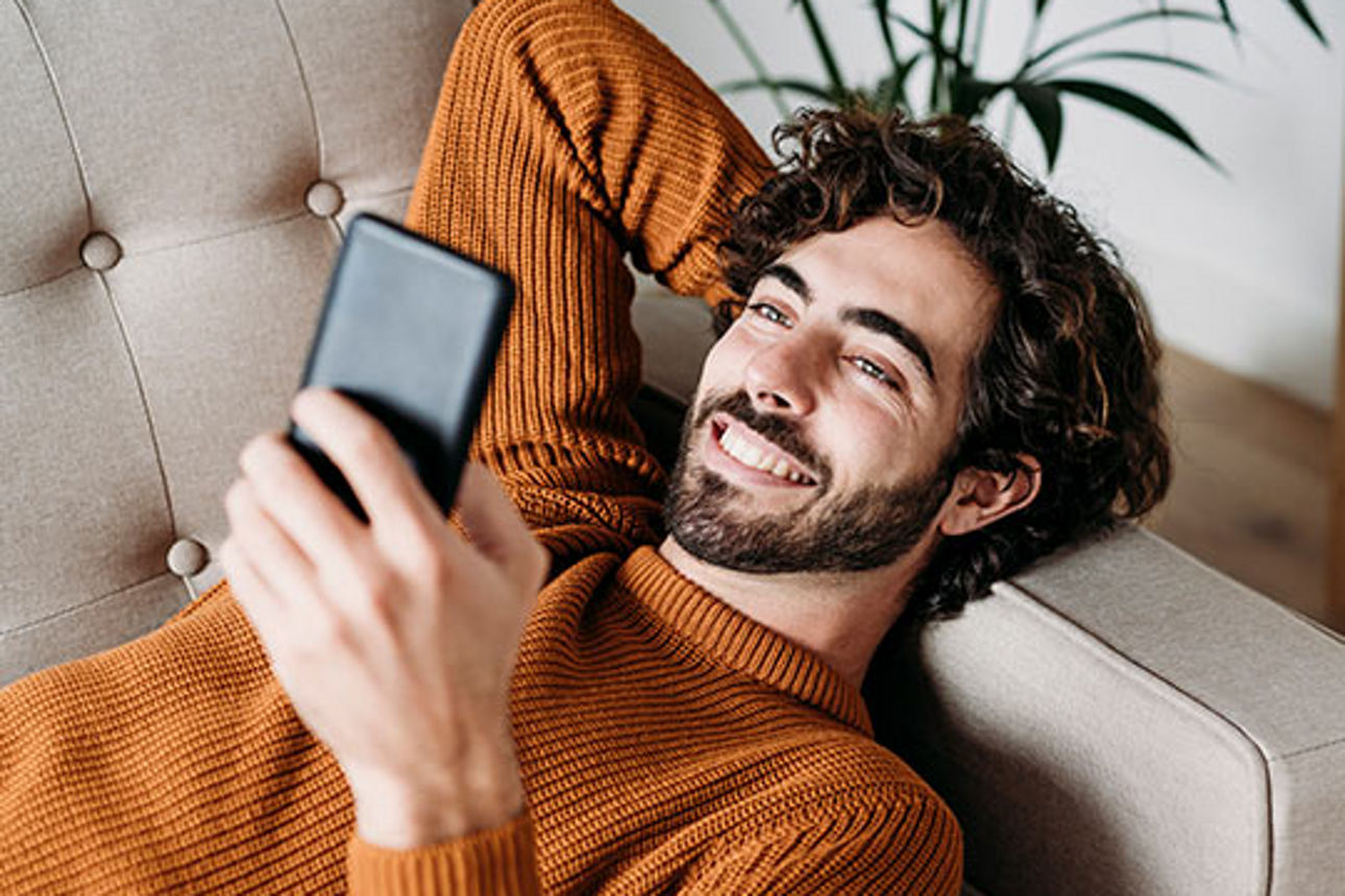 Junger Mann blickt erfreut in sein Smartphone