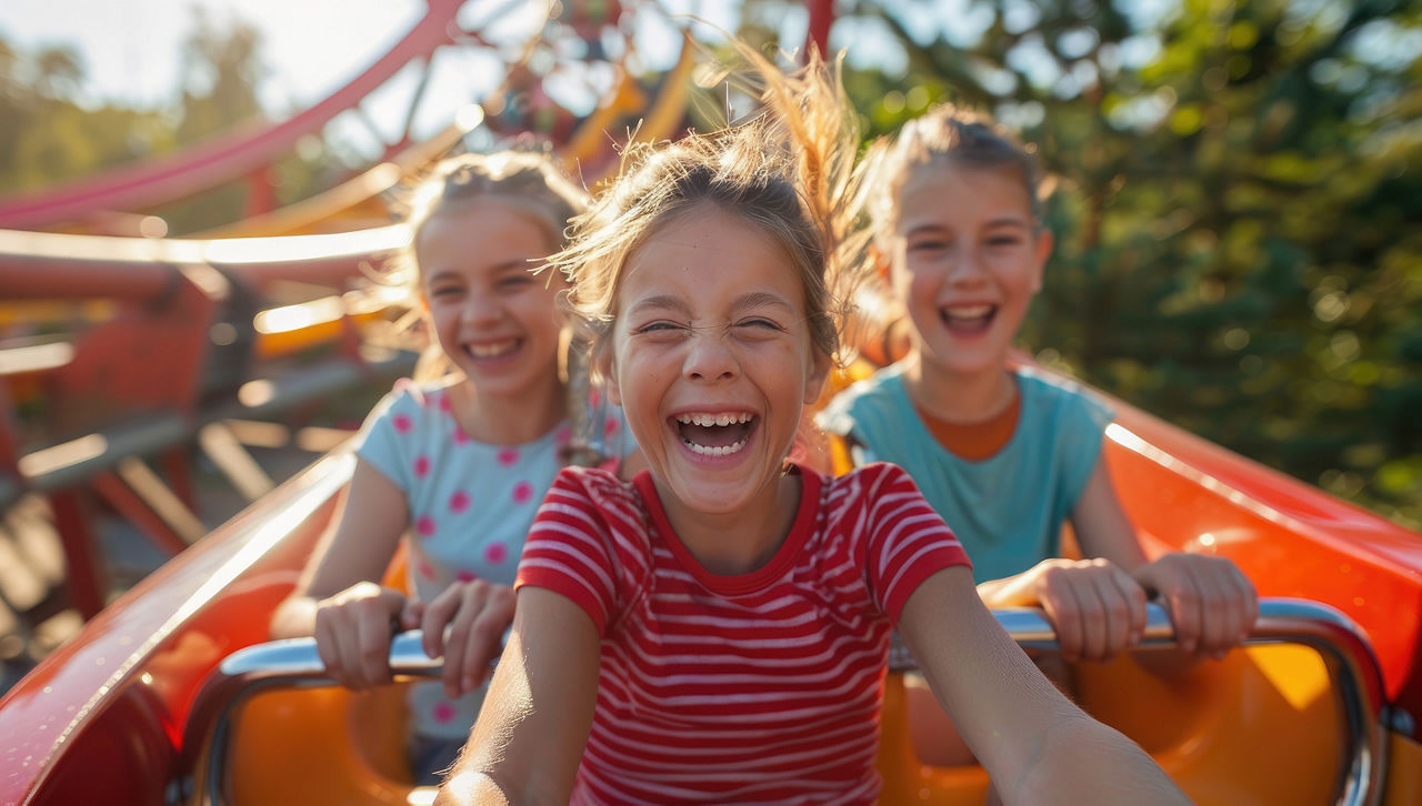 Two children ride a roller coaster at an amusement park at sunset. They have fun spending their summer holidays. Family weekend