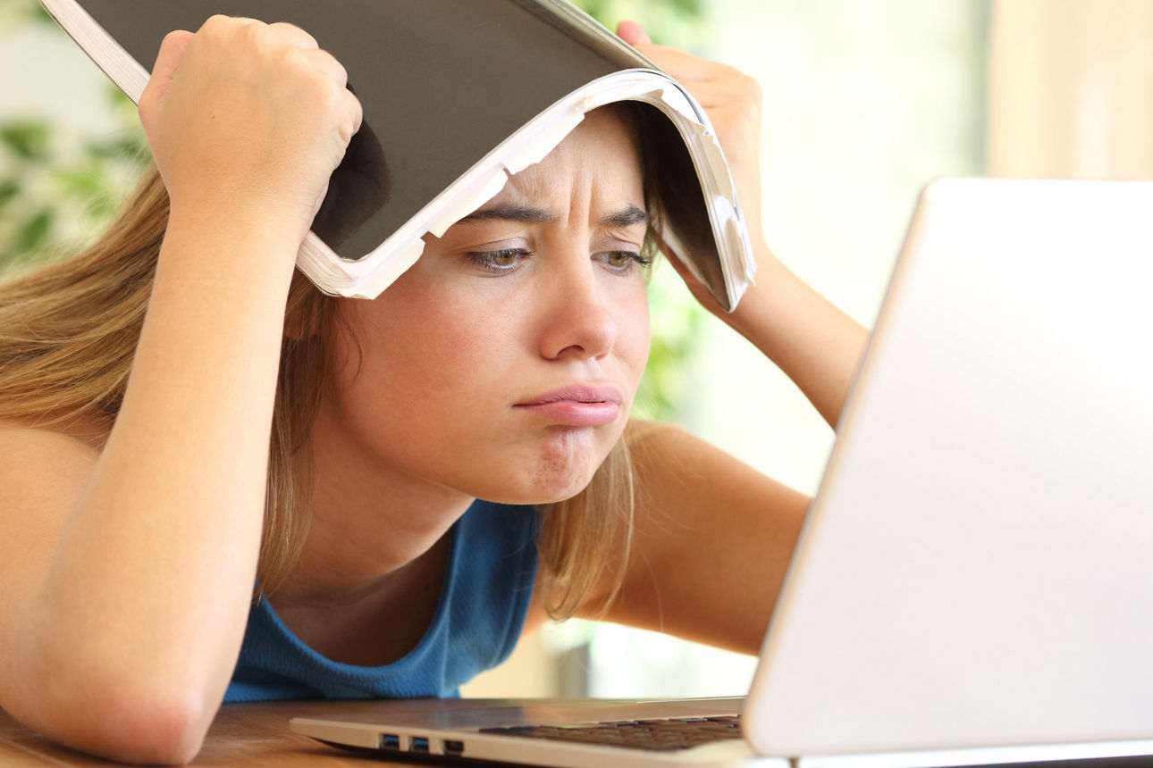 Schülerin bei den Hausaufgaben schaut frustriert in ihren Laptop.