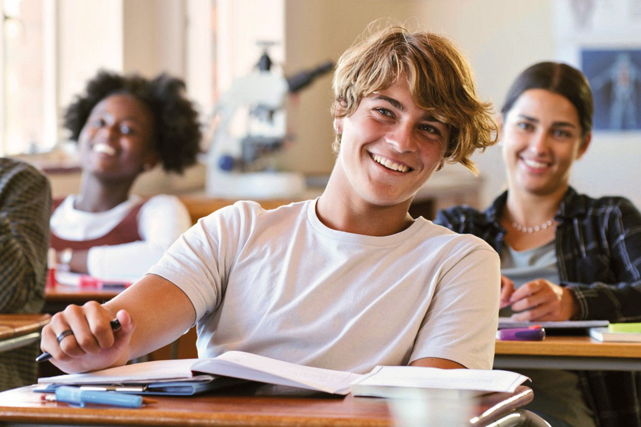 Schülerinnen und Schüler sitzen lächelnd in einem Klassenraum