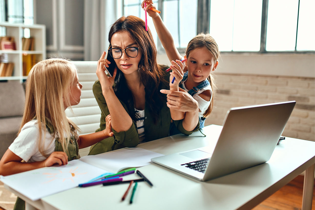 Mutter sitzt mit Schulkindern am Schreibtisch und macht Hausaufgaben