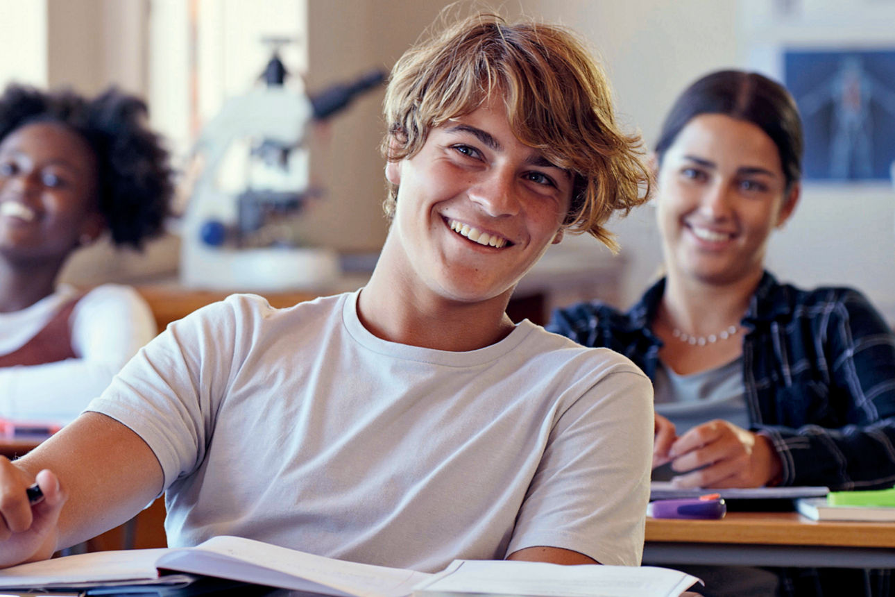 Schülerinnen und Schüler sitzen lächelnd in einem Klassenraum