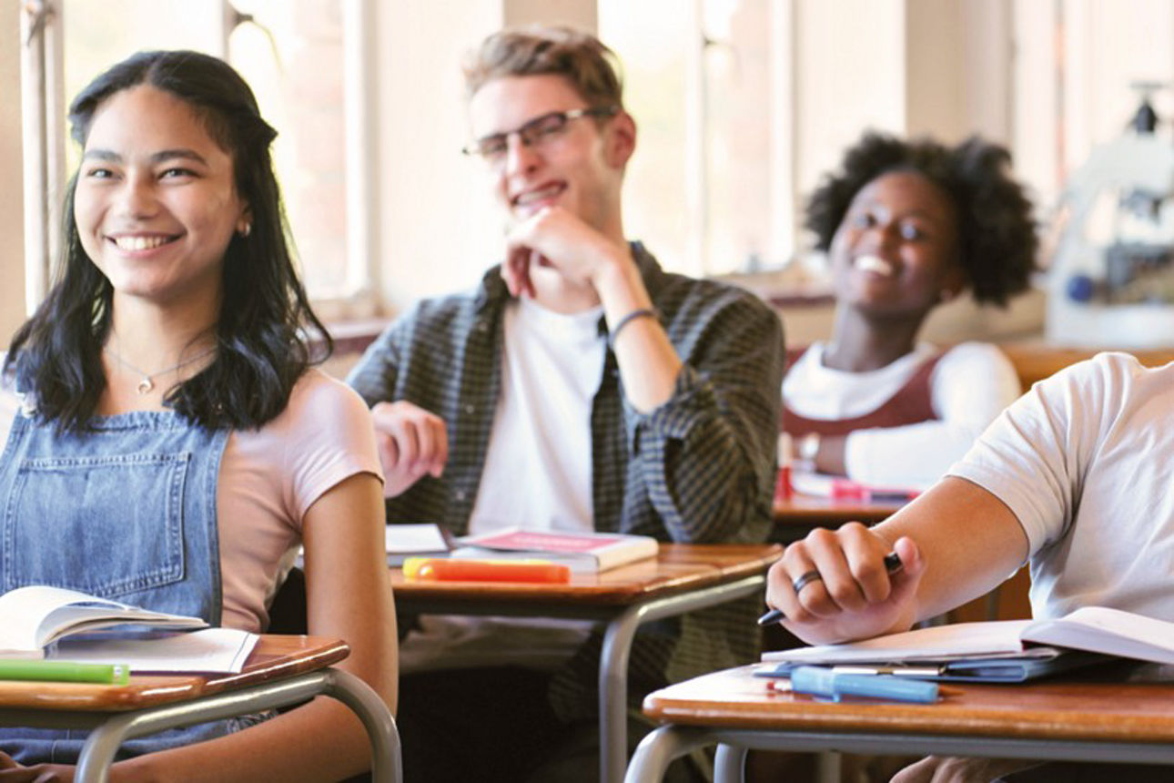 Schülerinnen und Schüler sitzen lächelnd in einem Klassenraum