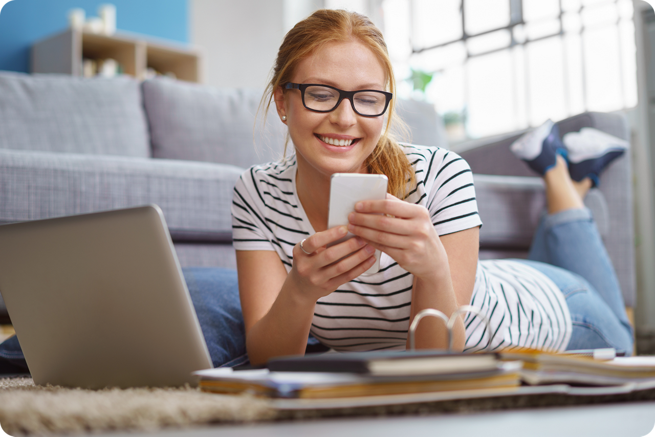Eine junge Frau liegt vor dem Sofa und hat ein Smartphone in der Hand