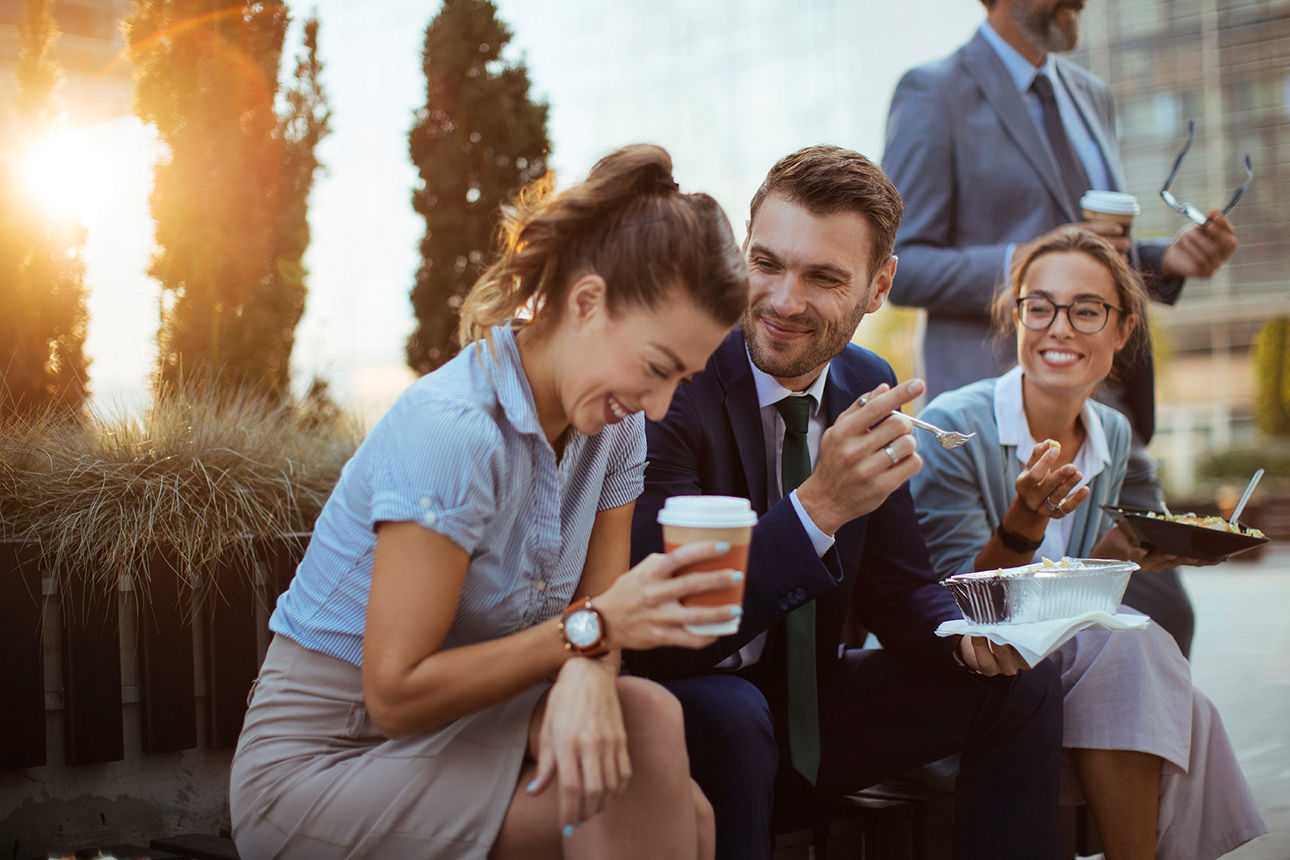 Lachende Menschen in Businesskleidung sitzen gemeinsam in der Mittagspause draußen