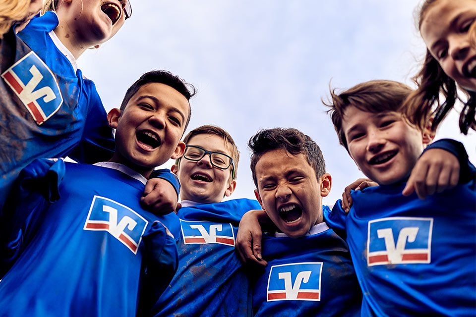 Lachende Gruppe von Kindern in Trikots mit dem Logo der Volksbanken Raiffeisenbanken