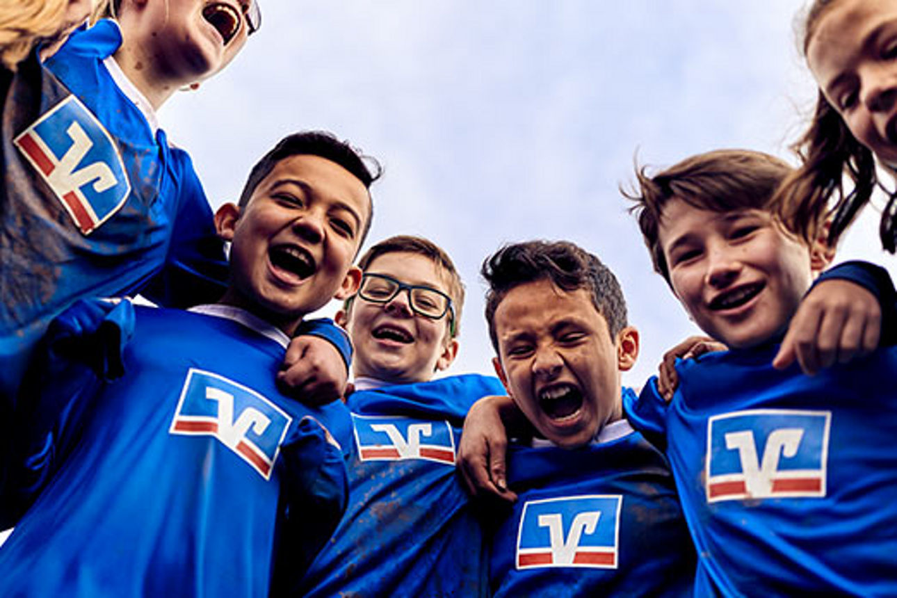Lachende Gruppe von Kindern in Trikots mit dem Logo der Volksbanken Raiffeisenbanken