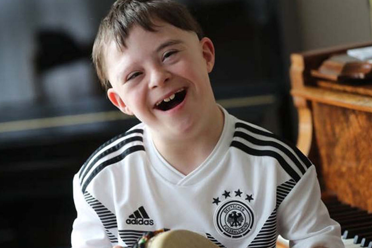 Junge mit Down-Syndrom lacht in die Kamera