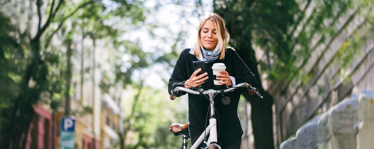 Junge Frau mit Handy und Kaffee am Fahrrad