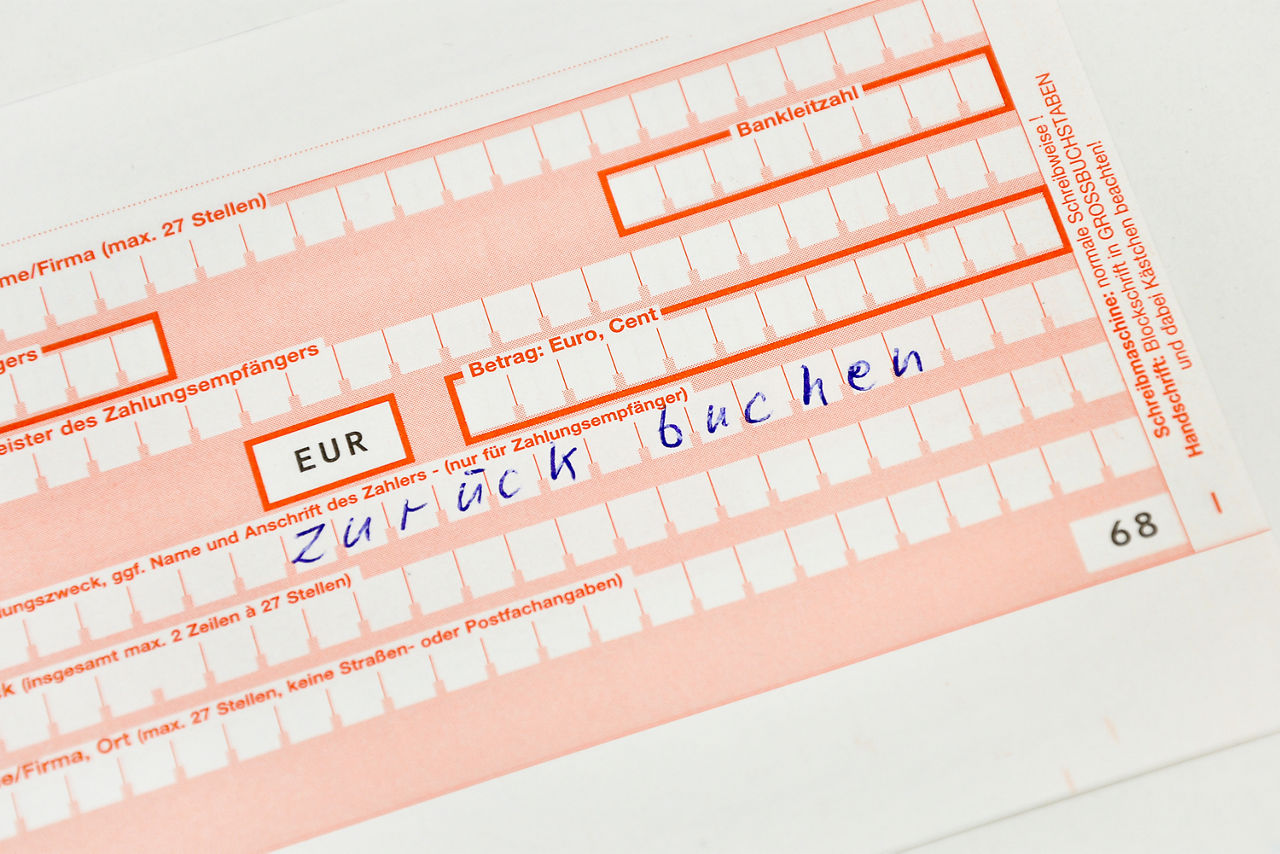 Das Bild zeigt einen Überweisungsschein, auf dem handschriftlich "zurück buchen" steht