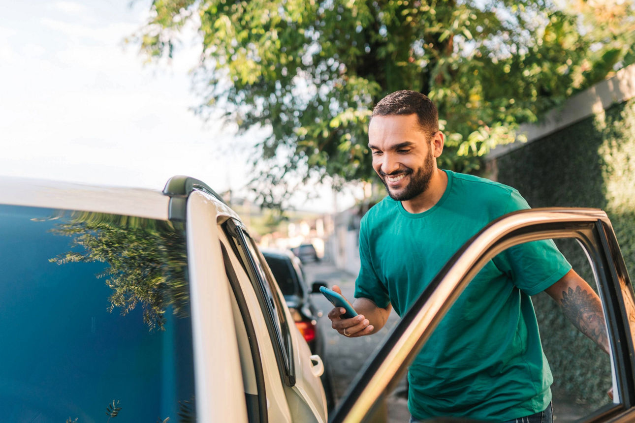 junger Mann mit Handy in der Hand steigt in ein Auto ein