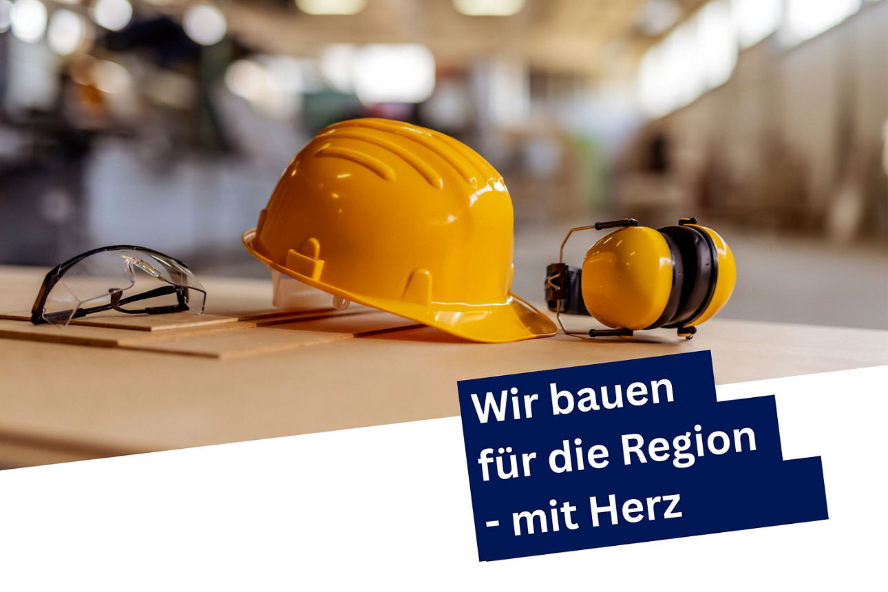 Ein Baustellenhelm auf einem Holztisch mit dem Text an der Seite "Wir bauen für die Region - mit Herz". 