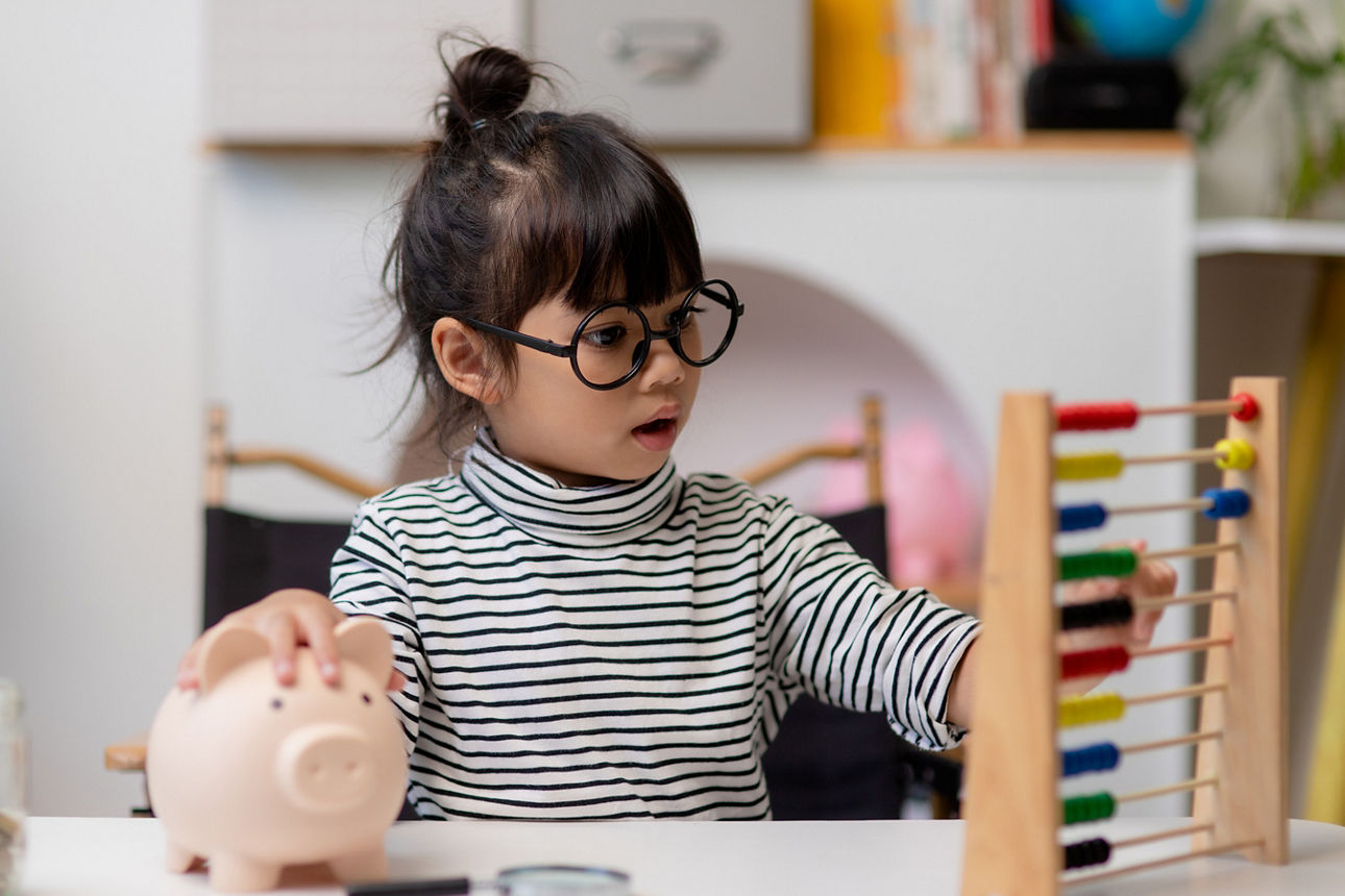 Ein Kind, dass den Umgang mit Geld mit einem Sparschwein und einem Rechenschieber lernt.