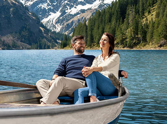 Ein Paar sitzt lachend auf einem Boot und treibt auf einem schönen Gebirgssee