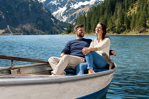 Mann und Frau sitzen entspannt in einem Paddelboot auf einem See, Berge im Hintergrund