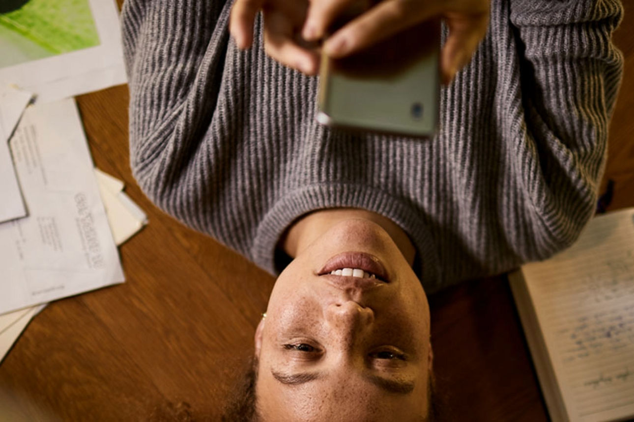 Eine junge Frau liegt mit dem Smartphone in der Hand auf dem Boden