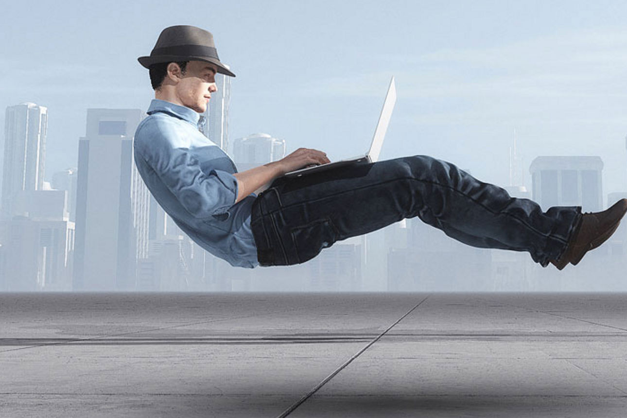 Mann schwebt mit Laptop auf dem Schoß vor einer Skyline