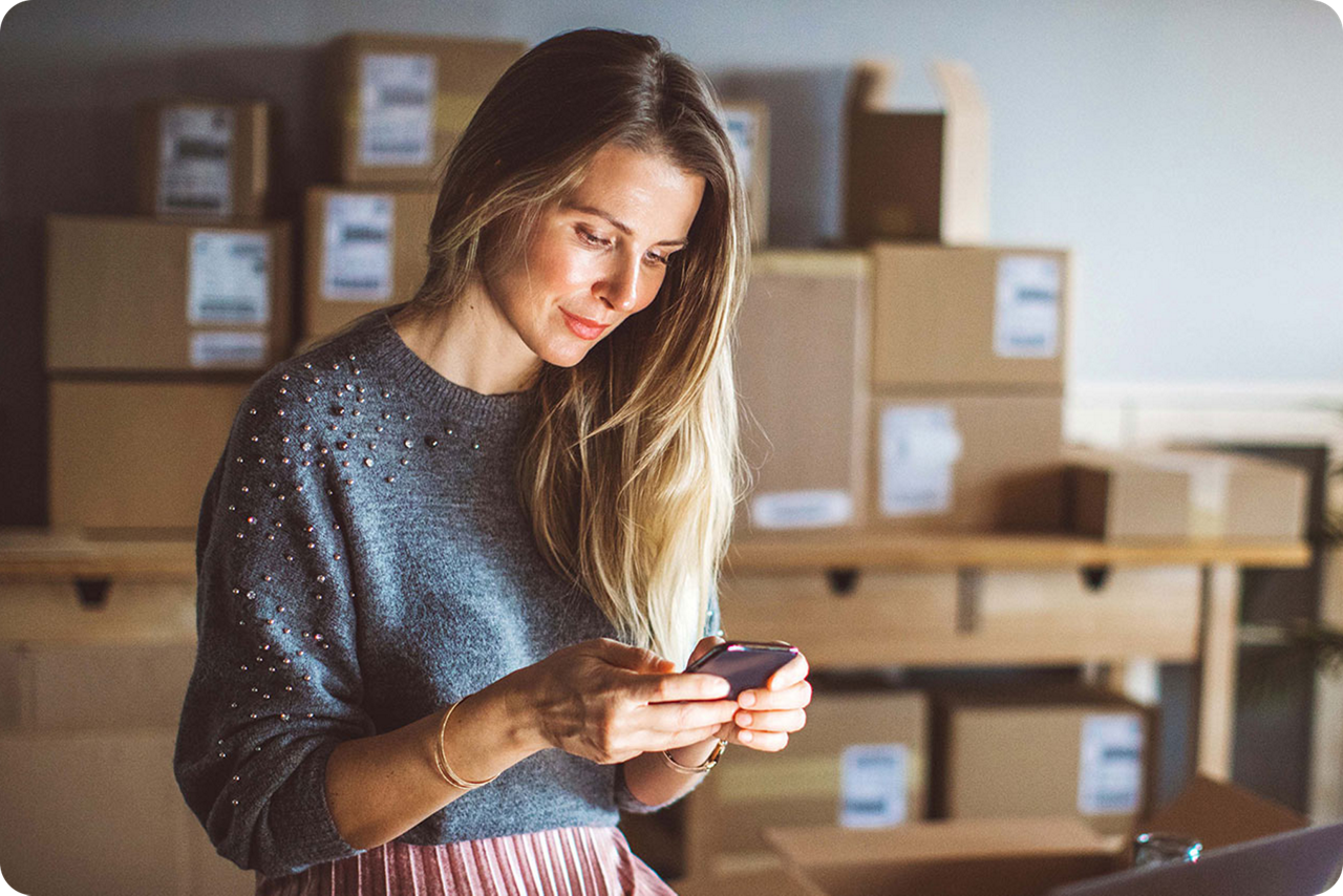 Eine Unternehmerin steht in ihrem Lager und schaut auf ihr Smartphone