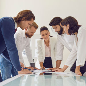 Eine gemischte Gruppe von Menschen die sich über einen Tisch beugen und gemeinsam nachdenken