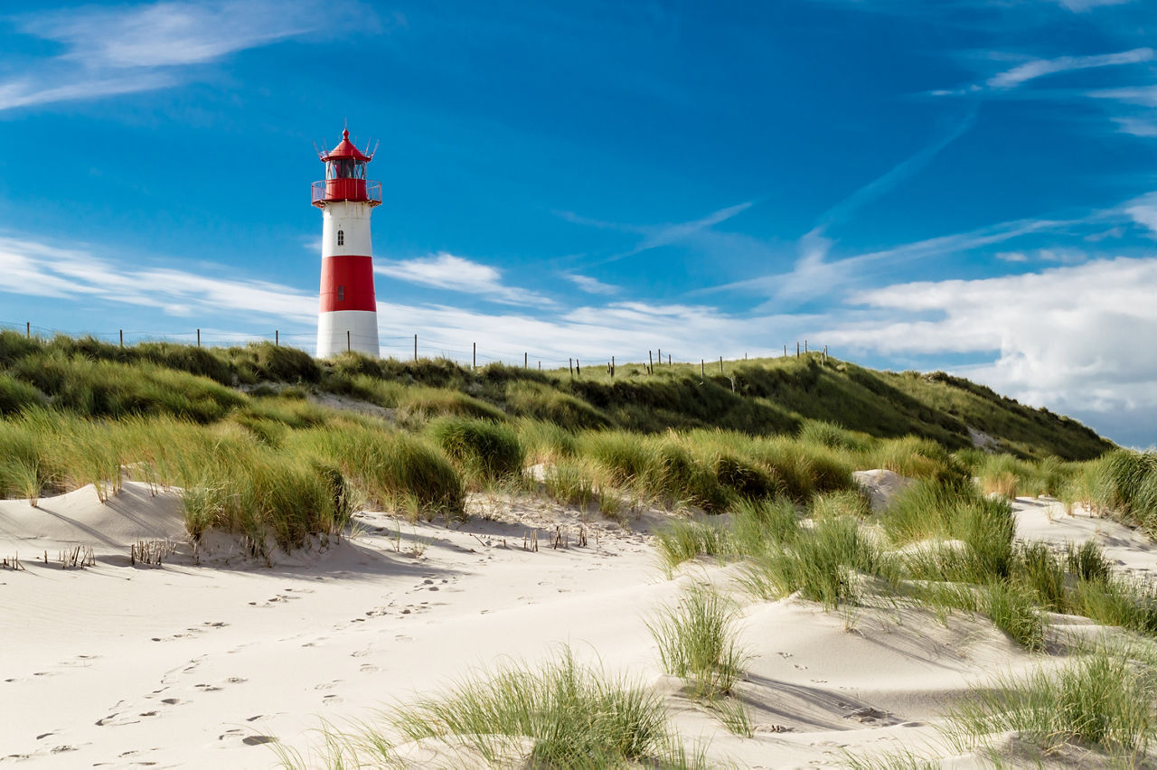 Roter Leuchtturm am Strand einer Küste mit grünen Gräsern und weißem Sand