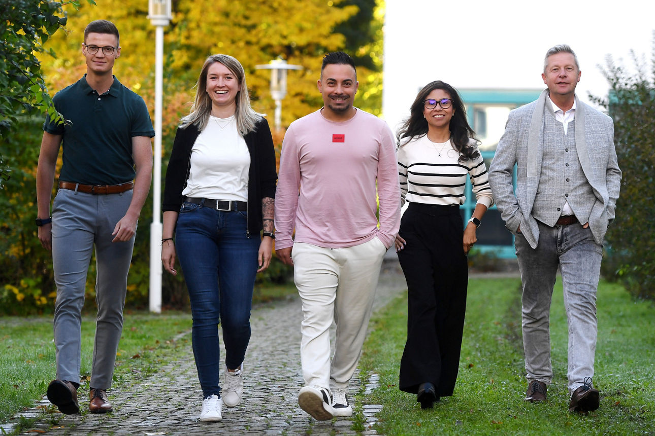 Eine Gruppe von fünf Erwachsenen, davon zwei Frauen und drei Männer laufen im freien und lachend auf den Kameramann zu.