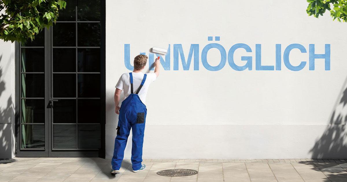 Junger Mann in Latzhose übermalt den Schriftzug „Unmöglich“ auf einer Wand