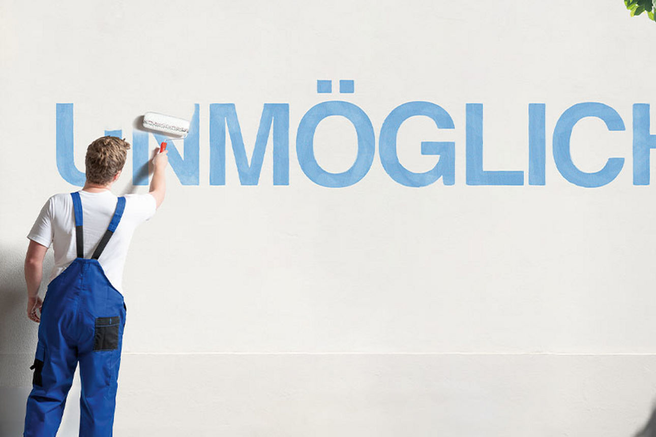 Junger Mann in Latzhose übermalt den Schriftzug „Unmöglich“ auf einer Wand
