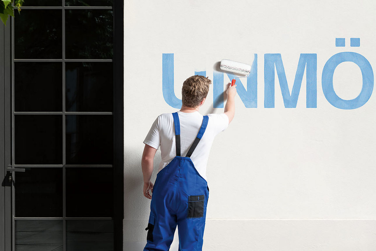 Junger Mann in Latzhose übermalt den Schriftzug "Unmöglich" auf einer Wand