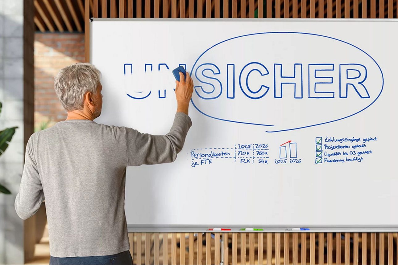 Ein Unternehmer steht vor einem Whiteboard und streicht die Buchstaben UN aus dem Wort UNSICHER