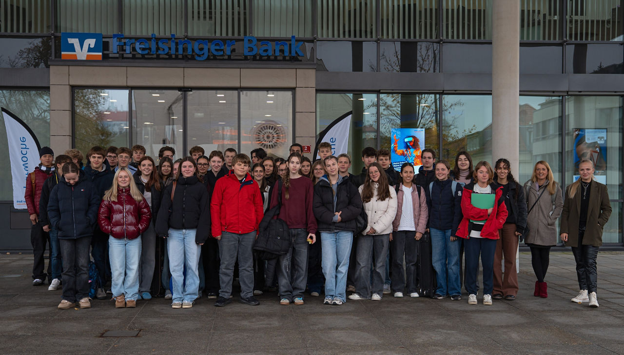 Gruppenfoto der Schüler/innen vor dem Eingang der Freisinger Bank mit Lehrerin und Alena Gula (Freisinger Bank)