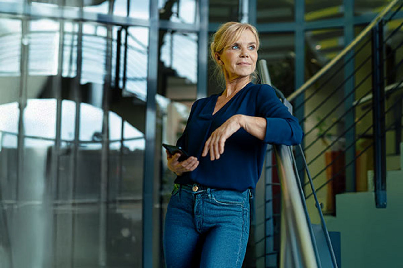 Eine lächelnde Frau steht in einem Firmengebäude auf einer Treppe