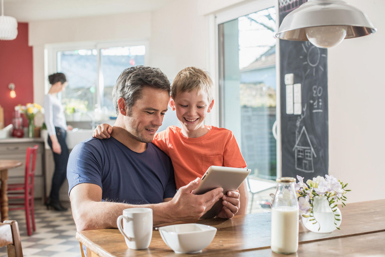 Vater und Sohn sitzen am Küchentisch und schauen auf ein Tablet