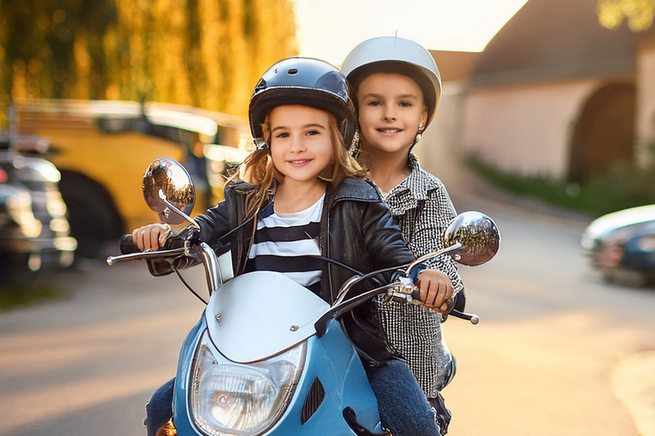 Ein Mädchen sitzt vorne auf einem Motorroller und ein Junge sitzt dahinter.