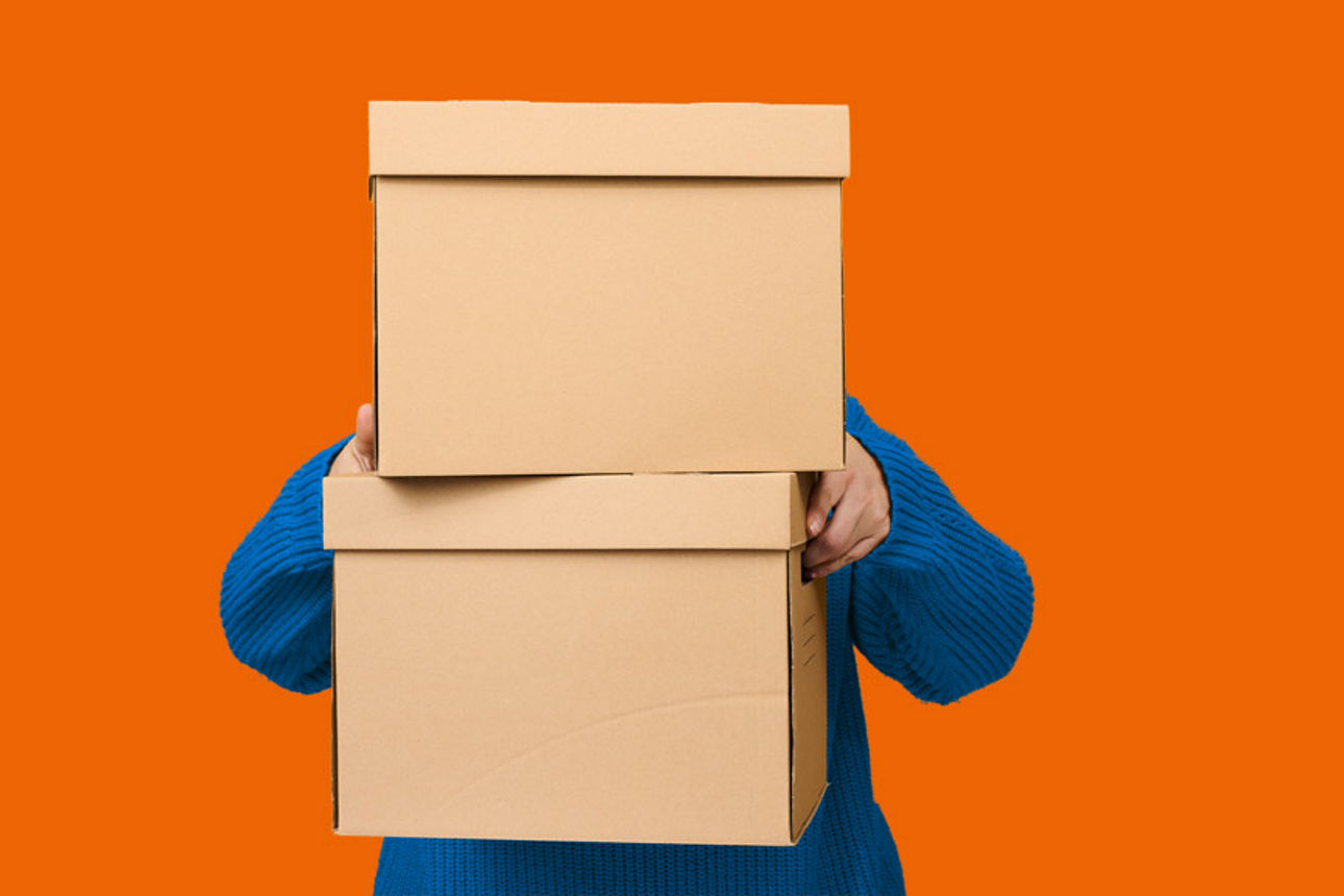 Eine Person beim tragen von Umzugskisten vor einem orangenen Hintergrund. 