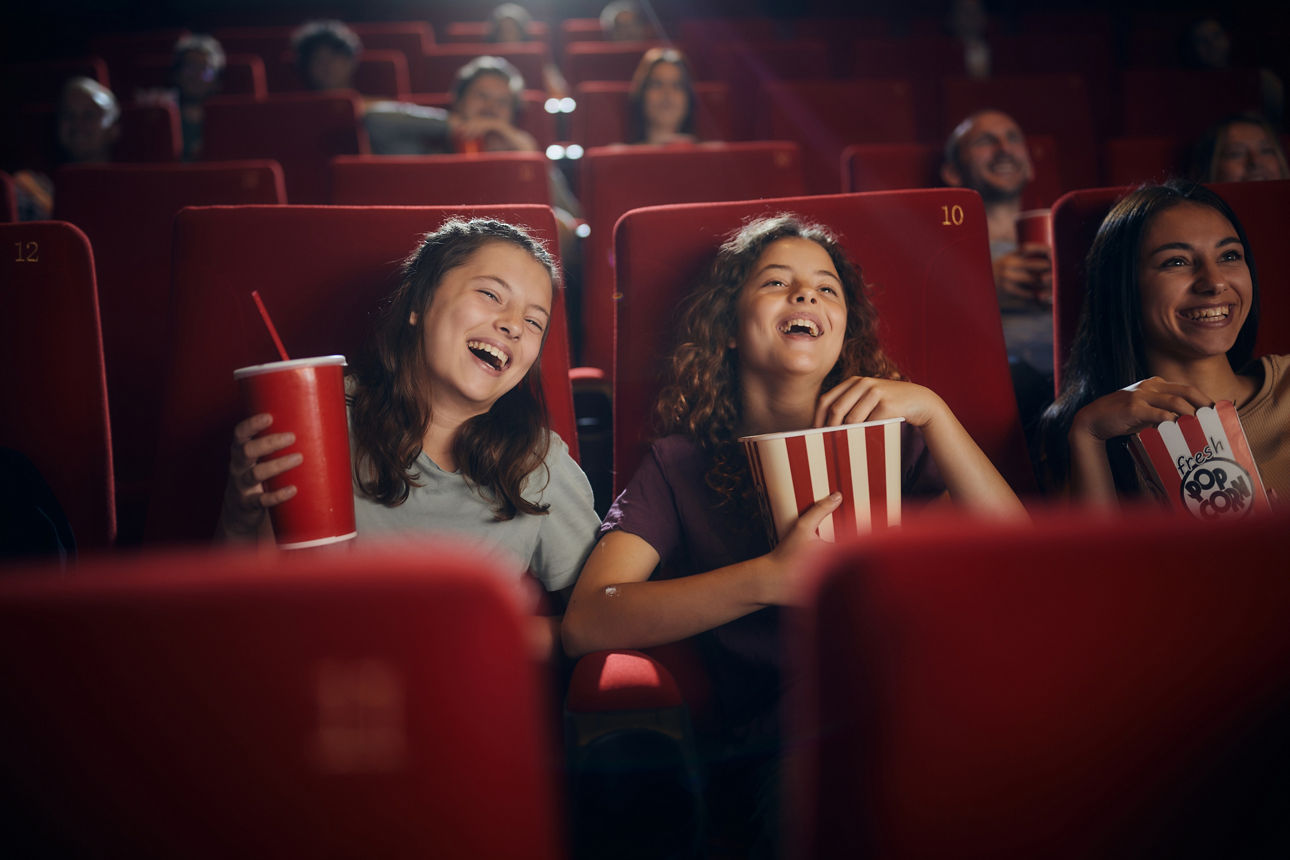 Drei glückliche junge Mädchen im Kino mit Popcorn und einer Cola. 