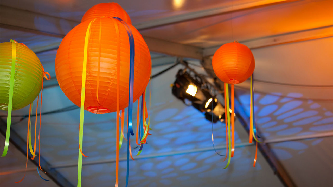 Bunte Lampinons und Luftschlangen hängen von einer Zeltdecke, die mit blauen Strahlern beleuchtet wird