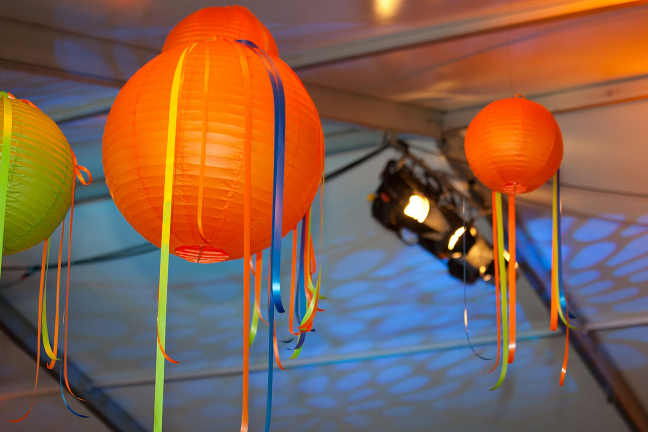 Bunte Lampinons und Luftschlangen hängen von einer Zeltdecke, die mit blauen Strahlern beleuchtet wird