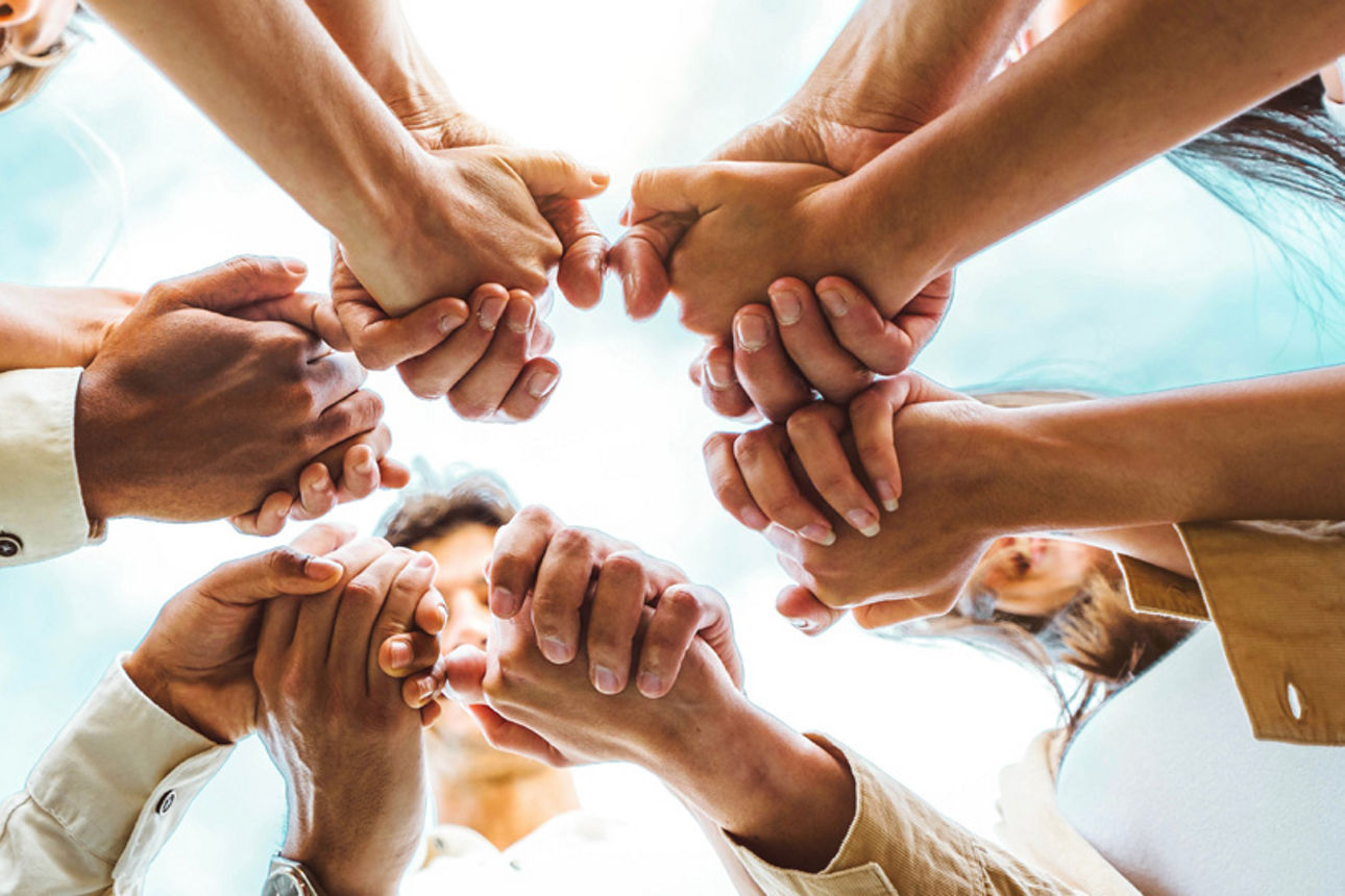 Gruppe junger Menschen steht im Kreis und hält sich an den Händen. 