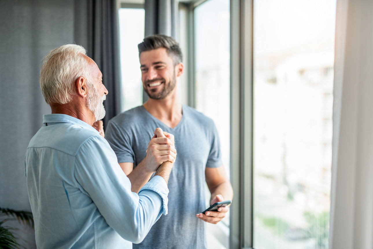 Vater und Sohn geben sich ein High-Five und schauen sich vor einem Fenster in die Augen