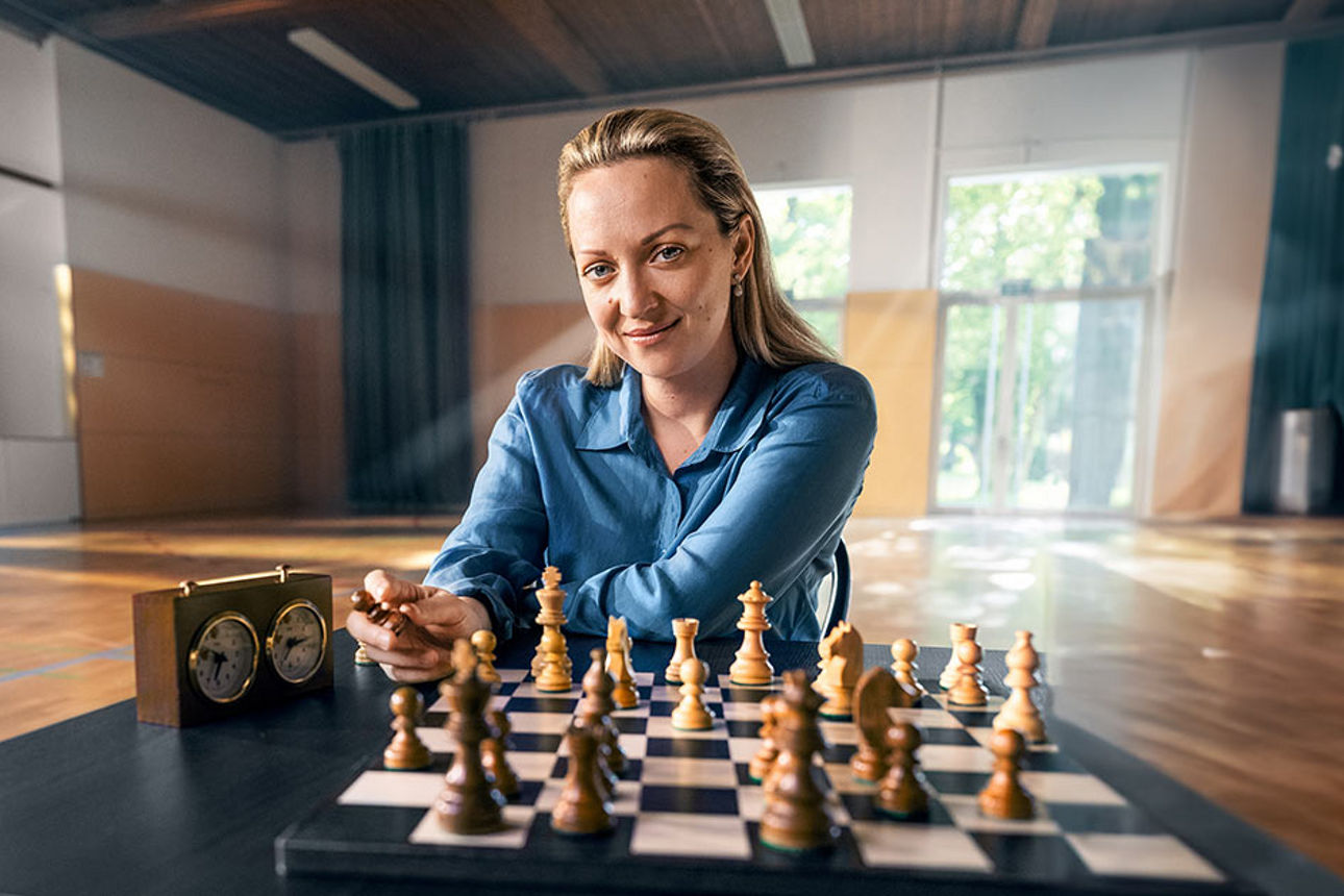 Die Schachspielerin Elisabeth Pähtz sitz lächelnd vor einem Schachbrett mit Spielfiguren