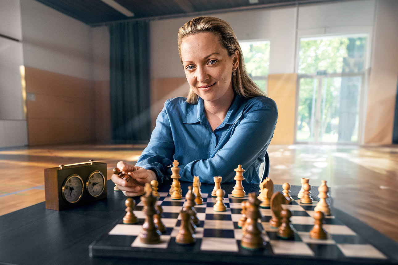 Die Schachspielerin Elisabeth Pähtz sitzt lächelnd vor einem Schachbrett mit Spielfiguren