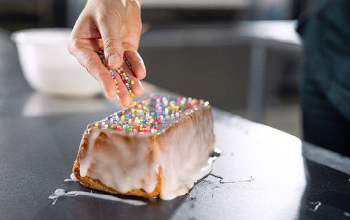 Ein Kuchen mit Zuckerguss, der mit bunten Perlen bestreut wird
