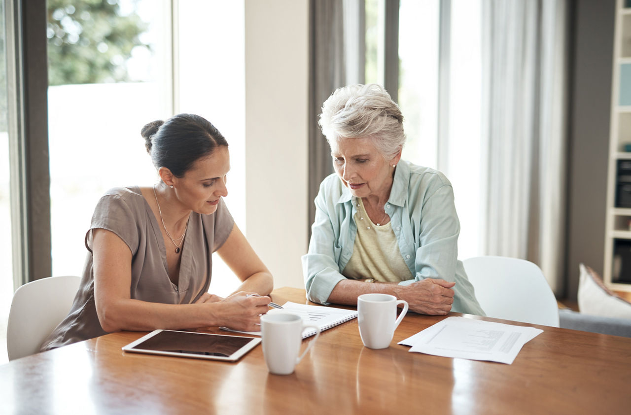 Eine jüngere und eine ältere Frau sitzen gemeinsam am Tisch und besprechen ihre Finanzen