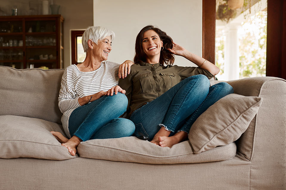 Frauen zweier Generationen sitzen lachend auf einem Sofa